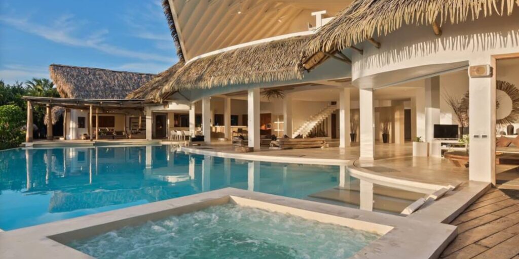 Thatched-roofed resort patio space around blue pool and hot tub. 