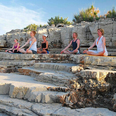 A group of yogis sit in lotus pose on a rocky plateau.