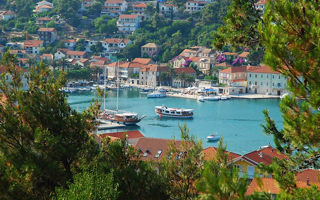Boats float in an urban harbour, with red-thatched-roof houses arrayed along the surrounding coast.